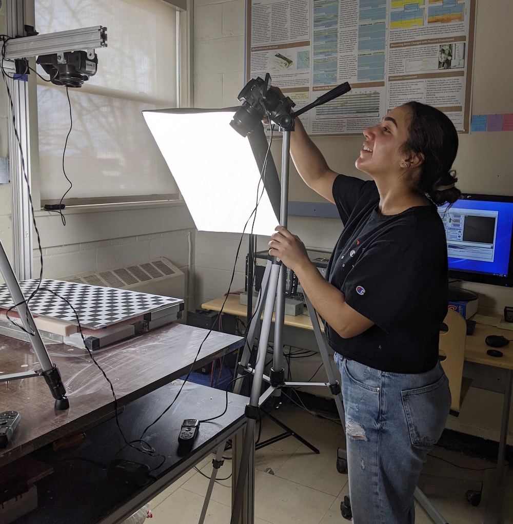 Latina woman with hair tied back is settting up cameras around the experimental set up